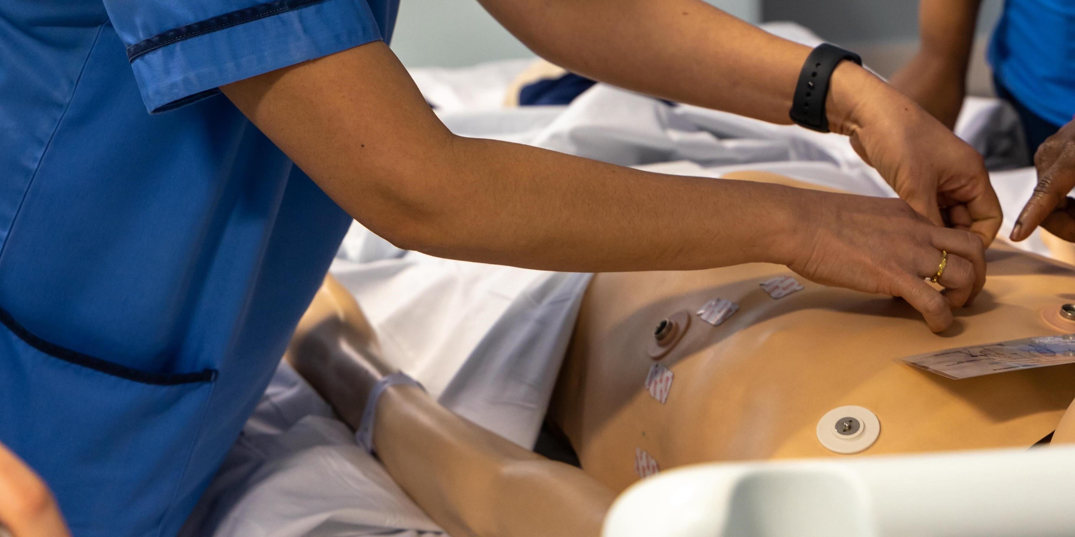 A student practicing the placement of ECG electrodes on a manikin