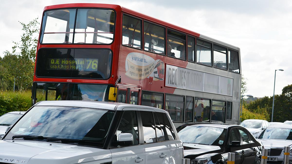 A double decker bus and several cars on the road outside QEHB