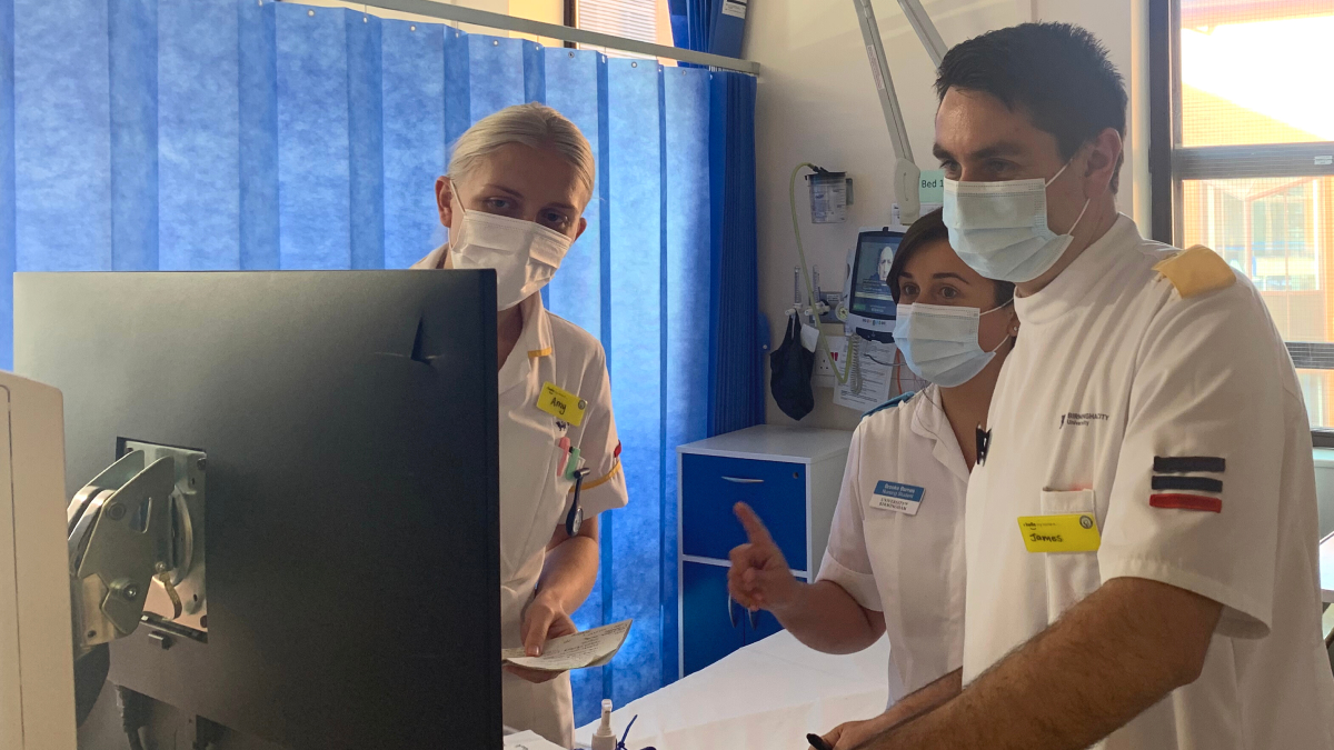 A female nurse instructing one male and one female student as they look at a computer screen