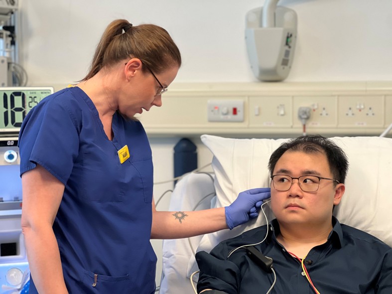 Healthcare professional placing an ear sensor on a participant during a clinical assessment in a hospital setting.