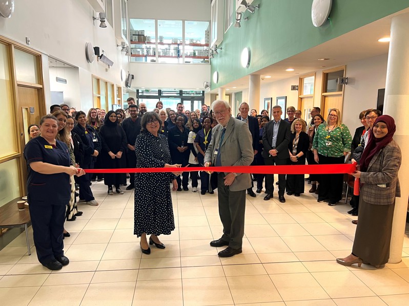 Two people cutting a red ribbon in front of a crowd of people